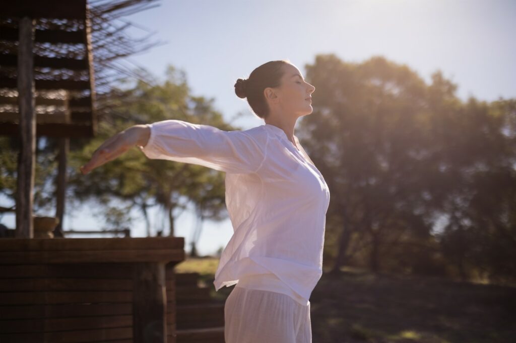 Une jeune femme effectue des mouvements de qi gong dans un parc, en début de matinée.